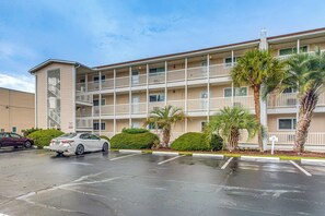 A multi-story building with balconies, a parking lot, and palm trees. - Walk to Ocean & Eats! Lake-view Myrtle Beach Haven (North Myrtle Beach)