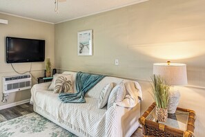 A living room with a sofa, a flat-screen TV, a wall-mounted air conditioner, a framed picture, a lamp, and a decorative plant. - Walk to Ocean & Eats! Lake-view Myrtle Beach Haven (North Myrtle Beach)