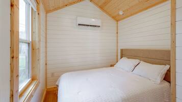 A bedroom with a bed, white bedding, a wooden ceiling, and an air conditioning unit.