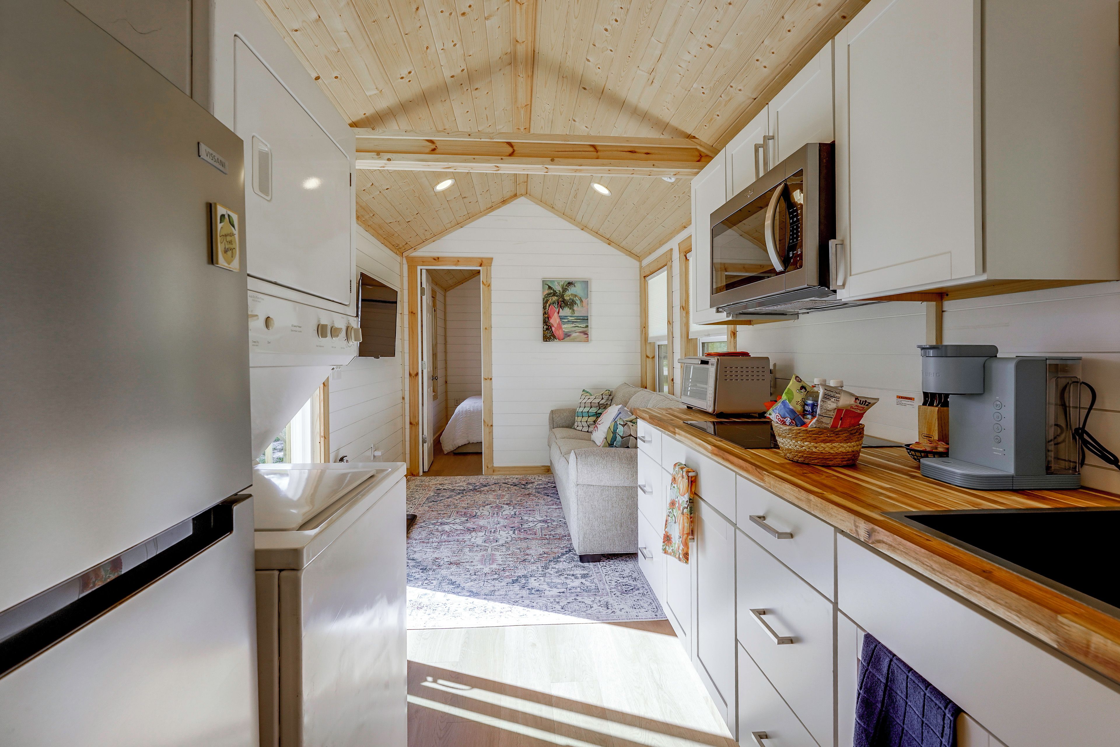 Une cuisine moderne avec des meubles blancs, un plafond en bois et une vue sur une chambre à coucher.