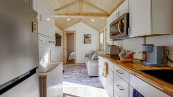 Une cuisine moderne avec des meubles blancs, un plafond en bois et une vue sur une chambre à coucher.