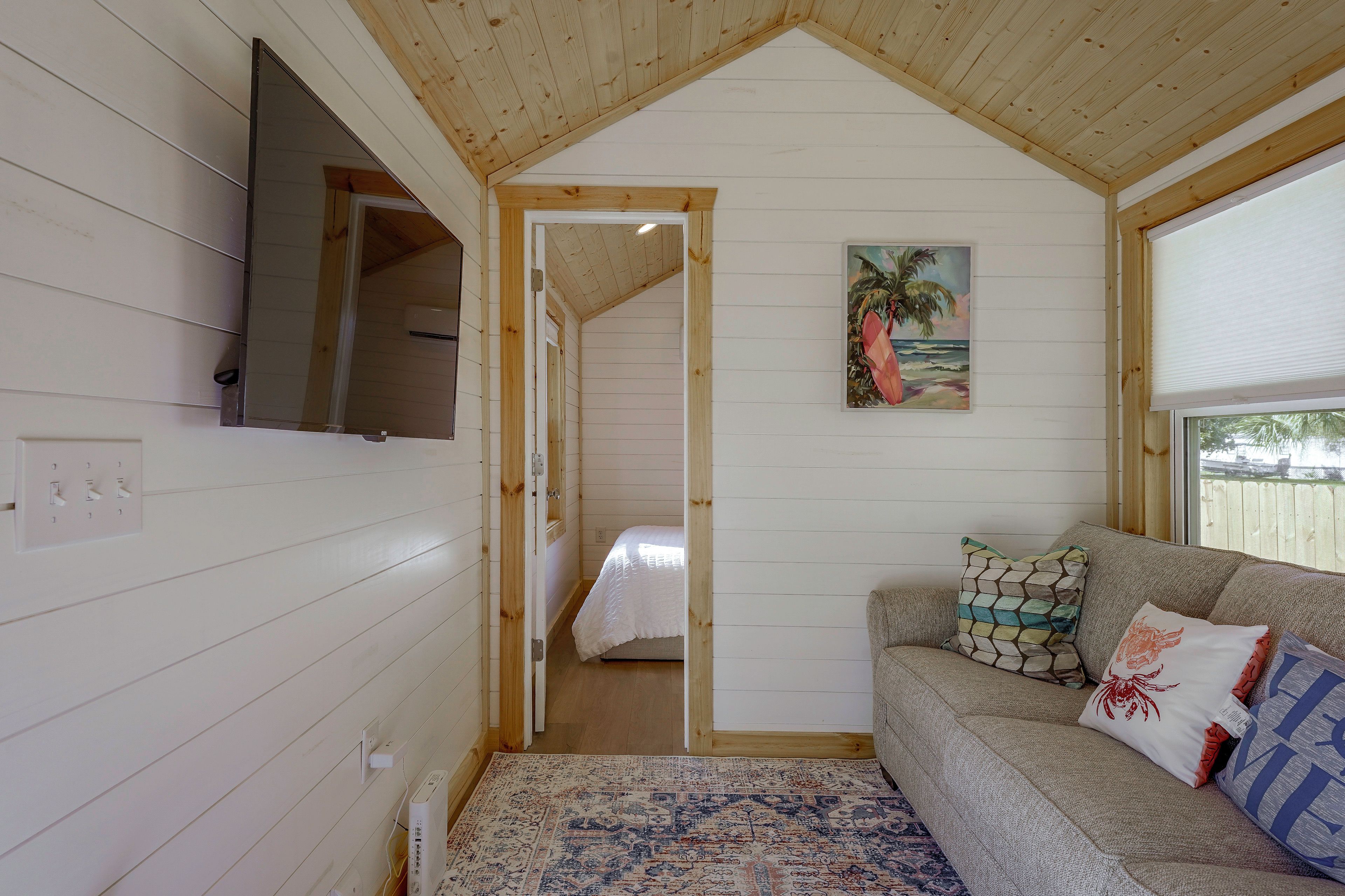 Une pièce chaleureuse avec un plafond en bois, un lit, un canapé agrémenté de coussins à motifs et un tableau représentant une scène de plage.