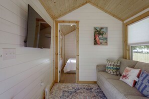 Una habitación acogedora con techo de madera, una cama, un sofá con cojines estampados y un cuadro de una playa.