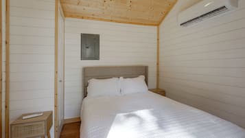 Un dormitorio con techo de madera, una cama con ropa de cama blanca, una mesita de noche y un aire acondicionado de pared.
