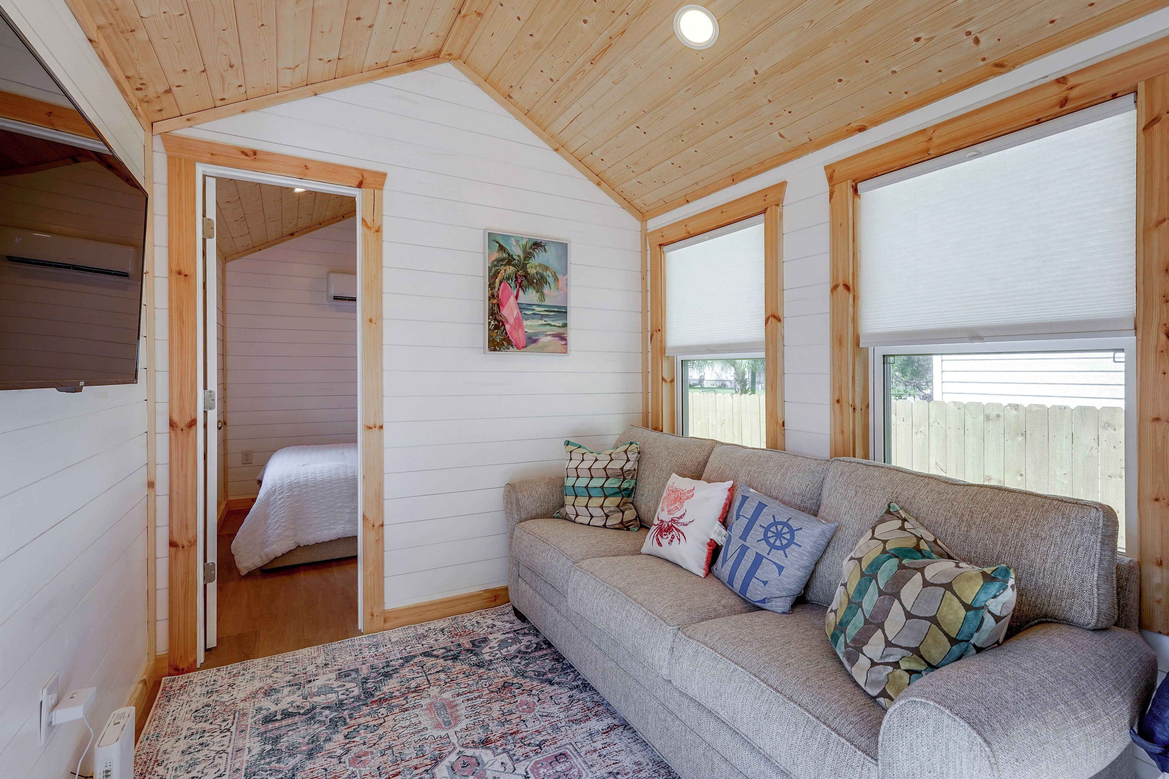 Ein gemütliches Zimmer mit Holzbalkendecke, einem Bett, einer Couch mit gemusterten Kissen und einem großen Fenster.