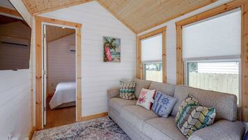 Ein gemütliches Zimmer mit Holzbalkendecke, einem Bett, einer Couch mit gemusterten Kissen und einem großen Fenster.