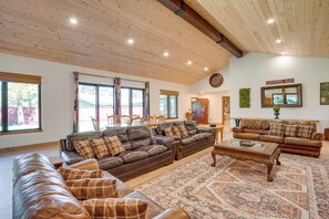 Ein geräumiges Wohnzimmer mit einer großen Ledersofa, einem kleineren Sofa und einem Couchtisch. Mehrere Fenster sorgen für natürliches Licht und einen Ausblick nach draußen.