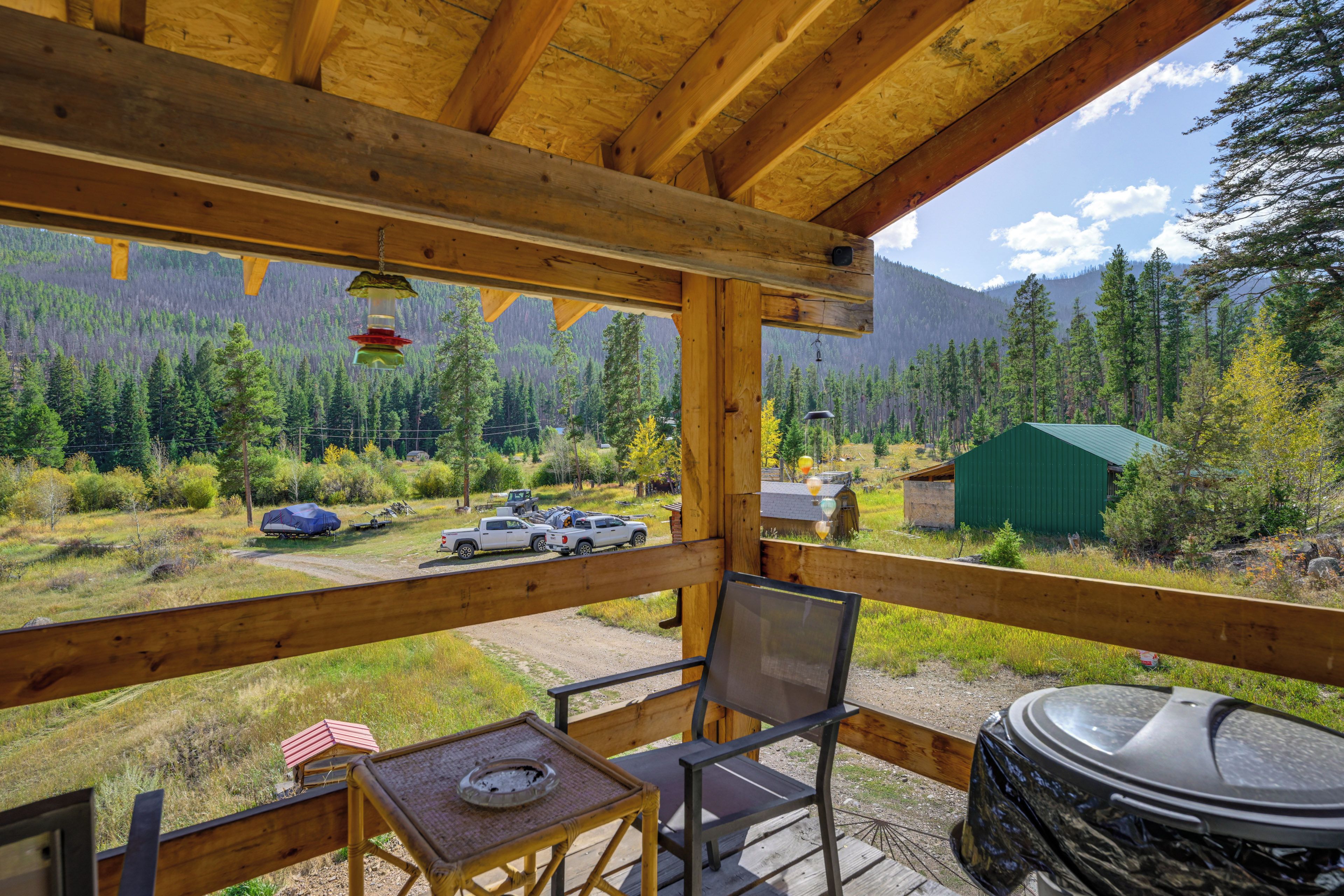 A wooden deck with a view of a forested mountain range, a covered picnic table, and a grill.