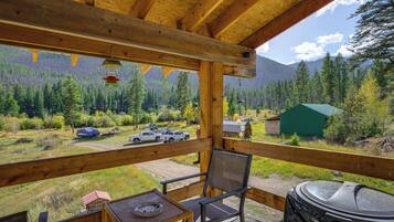 A wooden deck with a view of a forested mountain range, a covered picnic table, and a grill.