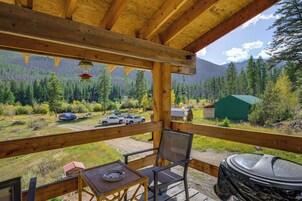 A wooden deck with a view of a forested mountain range, a covered picnic table, and a grill.