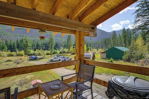 Une terrasse en bois offrant une vue sur une chaîne de montagnes boisées, une table de pique-nique couverte et un barbecue.