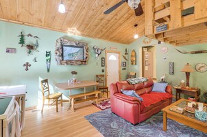 Una sala de estar acogedora con techo de madera, un sofá de cuero rojo, una mesa de comedor con sillas y diversas decoraciones en las paredes, incluyendo un cuadro enmarcado y un letrero.