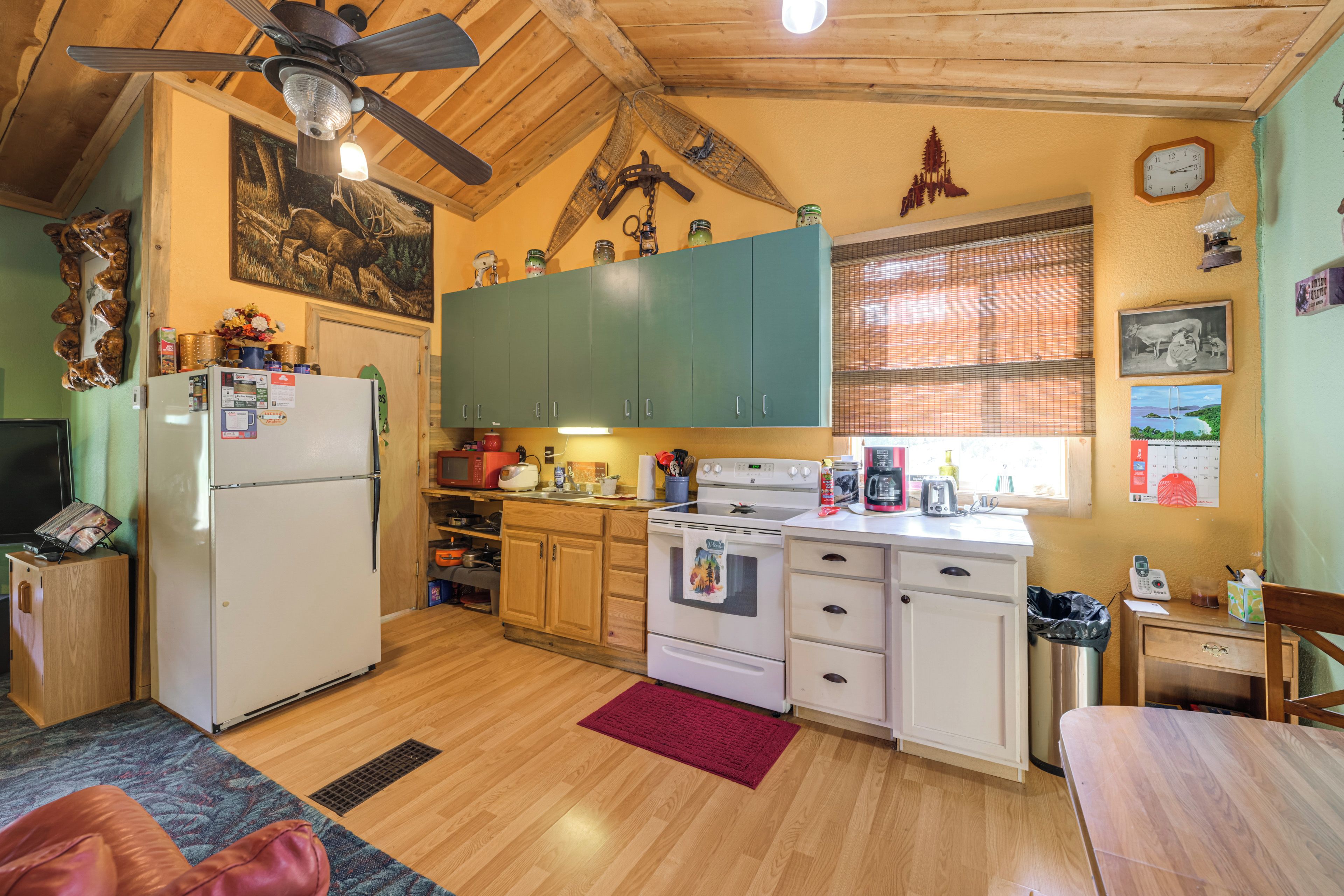 A compact kitchen with wooden cabinets, a refrigerator, a stove, and a ceiling fan.