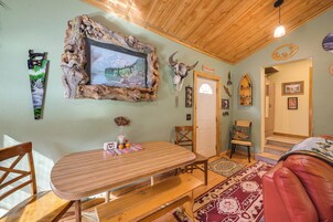 Un interior rústico con una mesa de madera, sillas, un televisor montado y diversas decoraciones en las paredes, incluyendo un cráneo y un cartel.