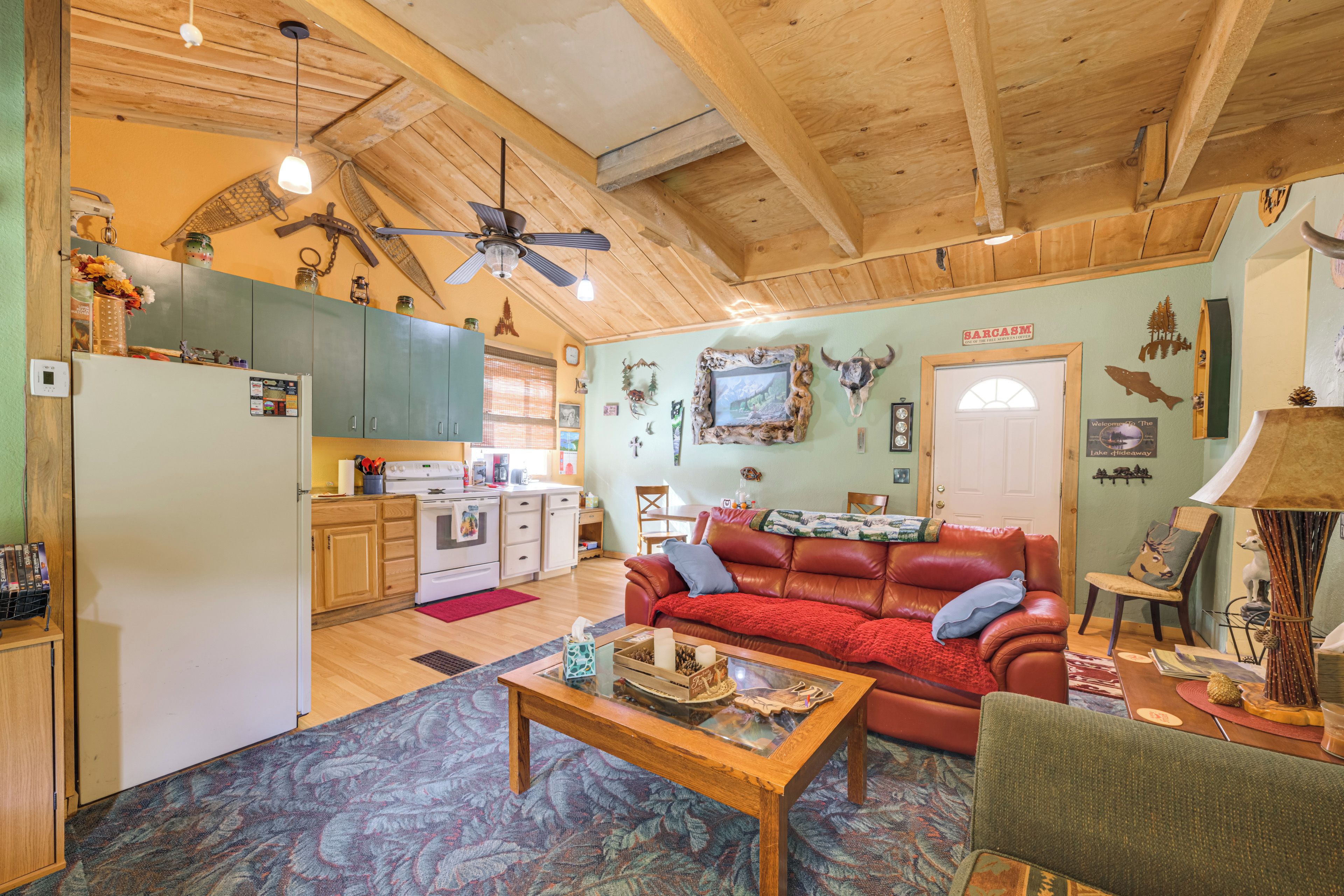 A cozy living room with a leather sofa, a wooden coffee table, and a kitchen area with wooden cabinets and a stove.