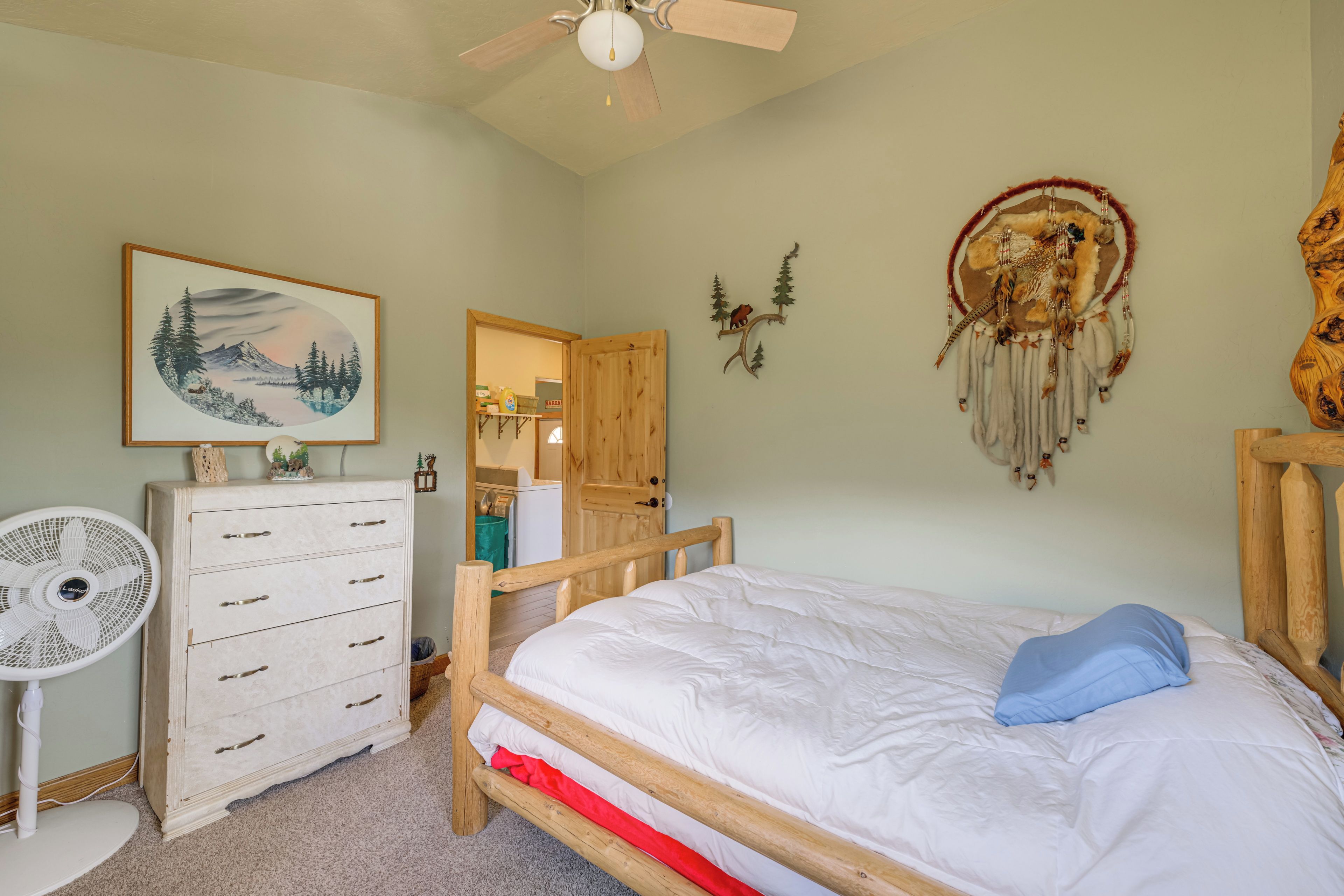A bedroom with a bed, dresser, fan, and wall art.