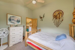 A bedroom with a bed, dresser, fan, and wall art.
