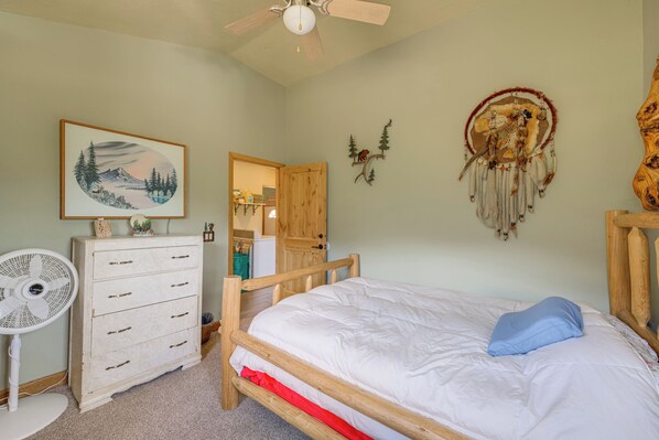 Une chambre à coucher avec un lit, une commode, un ventilateur et des œuvres d’art murales.
