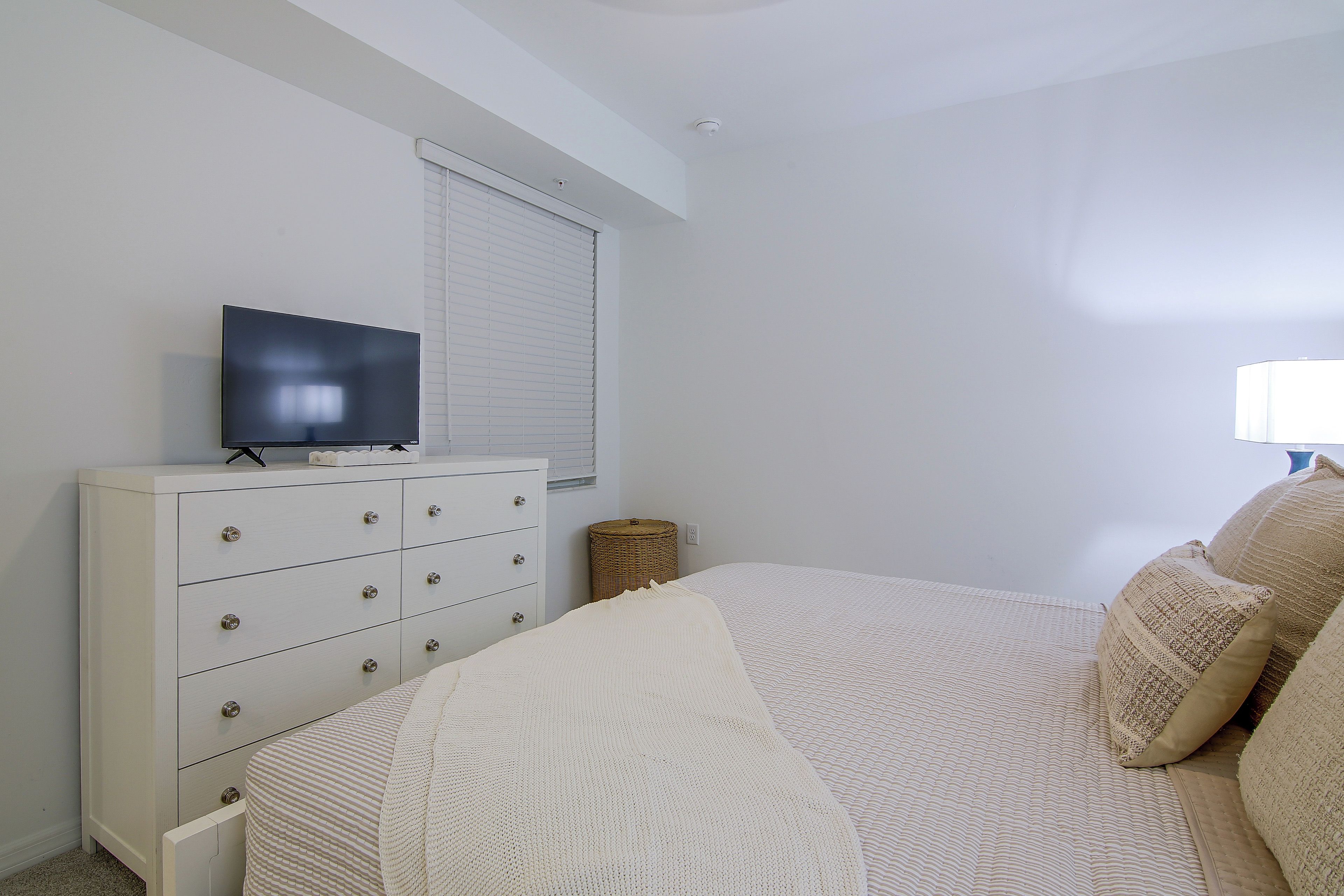 Quarto com cama, penteadeira, televisão e janela com persianas.