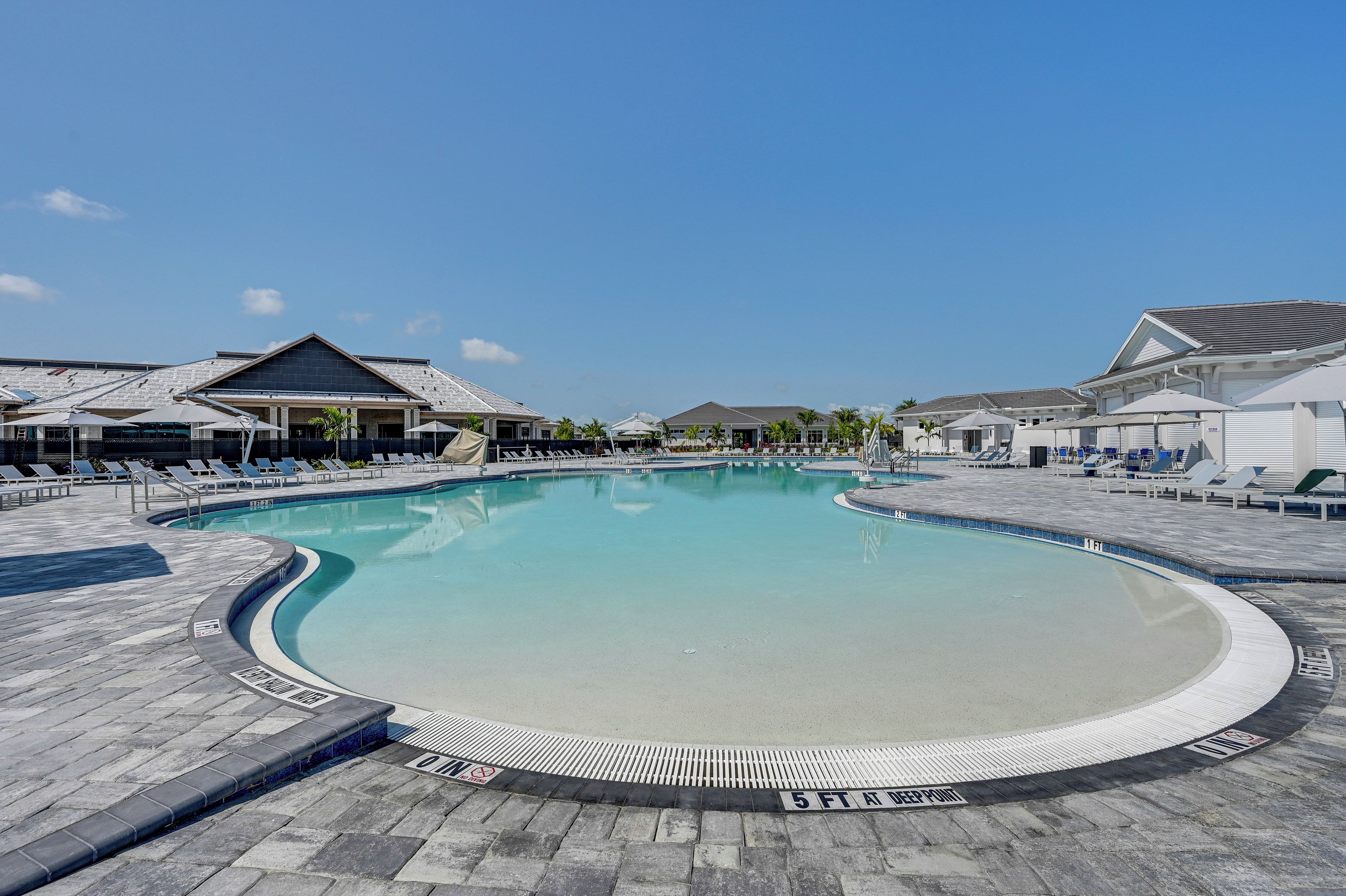 Uma piscina grande e curva com água azul cristalina, rodeada por espreguiçadeiras e guarda-sóis.