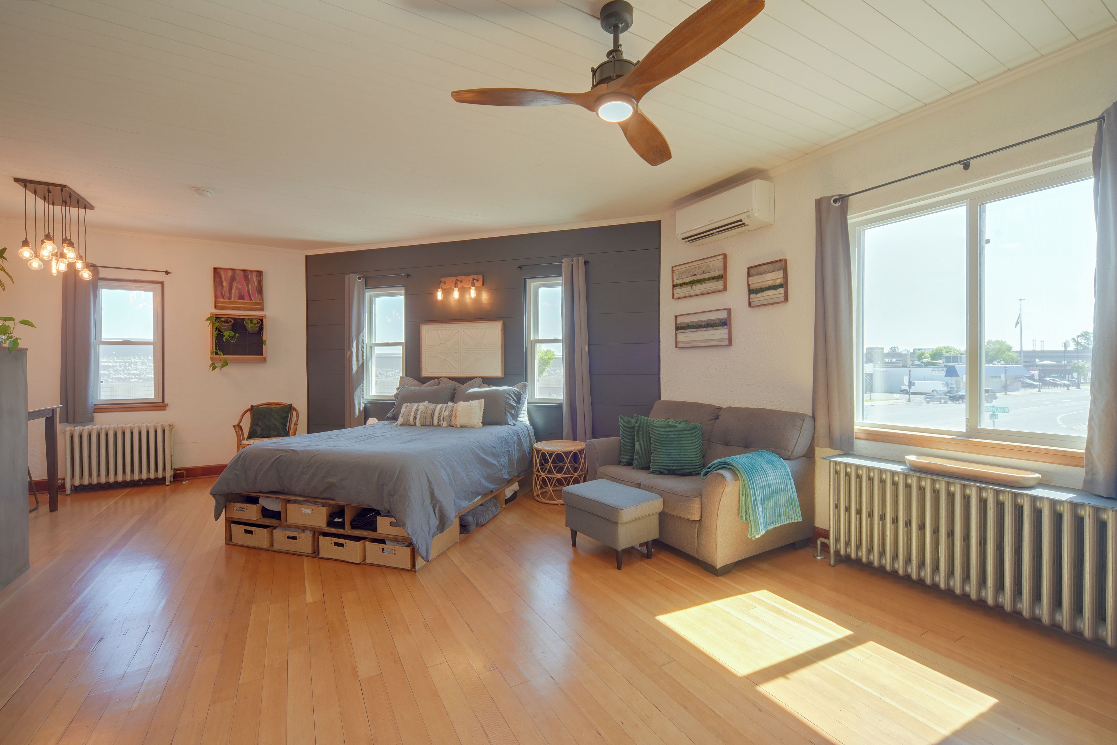 Une chambre à coucher comprenant un lit, un canapé, une chaise, un ventilateur de plafond et une fenêtre donnant sur la rue.