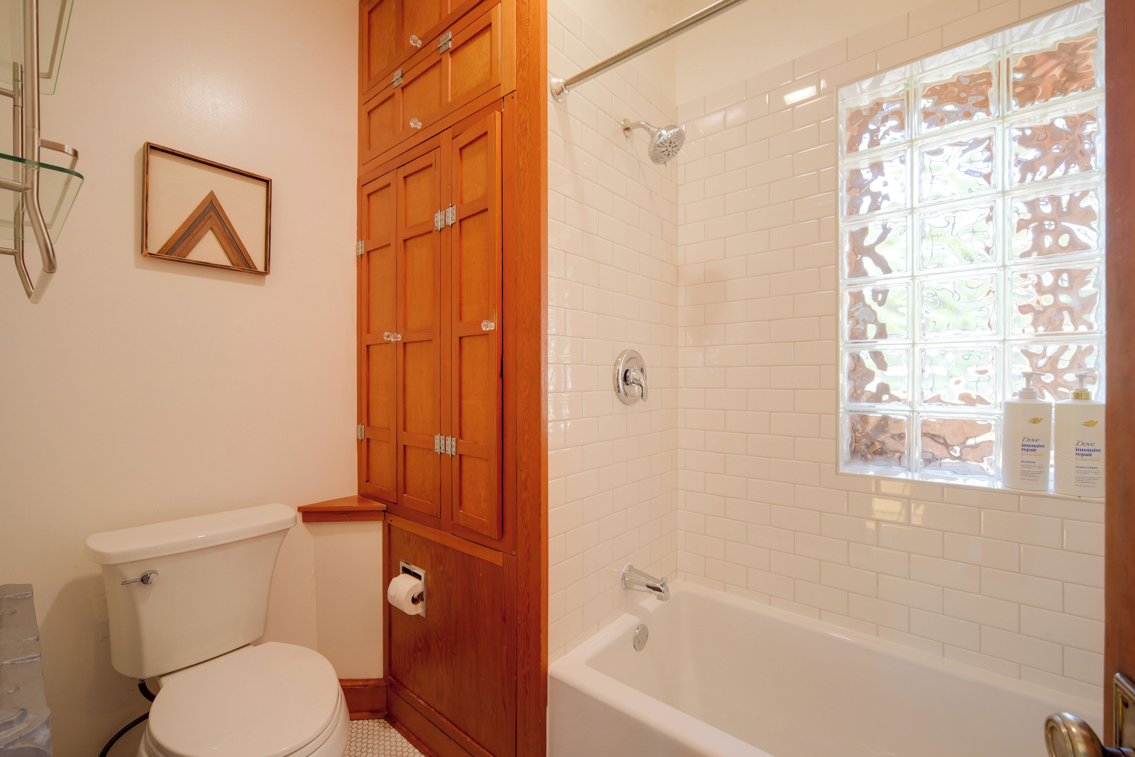 A bathroom with a toilet, wooden cabinets, a shower with a frosted glass window, and a bathtub.