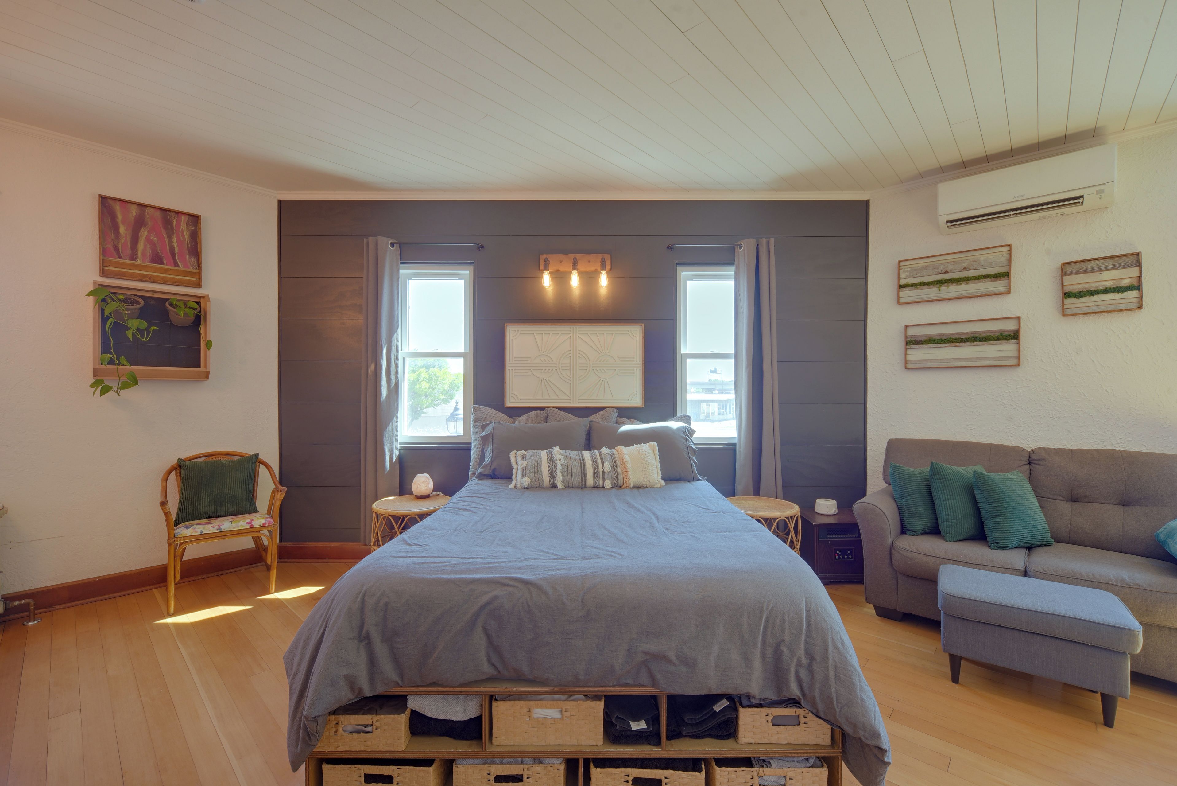 A bedroom with a bed, a nightstand, a chair, a sofa, and a wall with artwork.