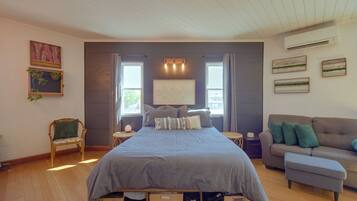 A bedroom with a bed, a nightstand, a chair, a sofa, and a wall with artwork.