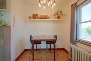 A dining area with a wooden table and chairs, a hanging light fixture, a shelf with decorative items, and a window with curtains. - Charming Couple's Gem in Duluth w/ Enclosed Porch (Duluth)