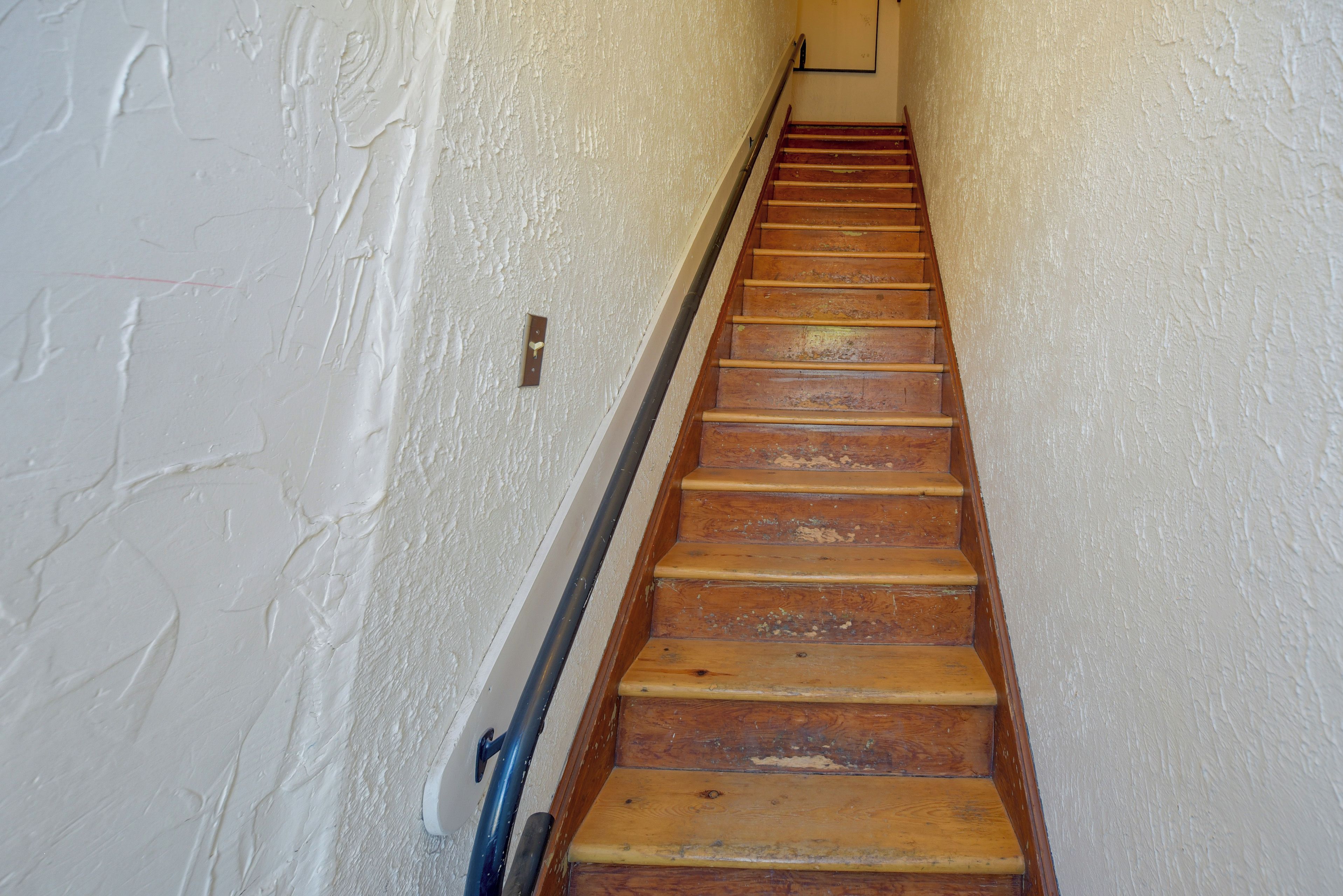 A wooden staircase with a handrail, leading upwards.