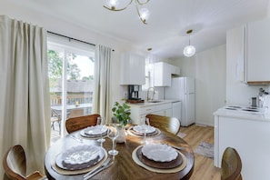 Un comedor con una mesa preparada para cuatro, una cocina al fondo y vistas al exterior a través del ventanal.