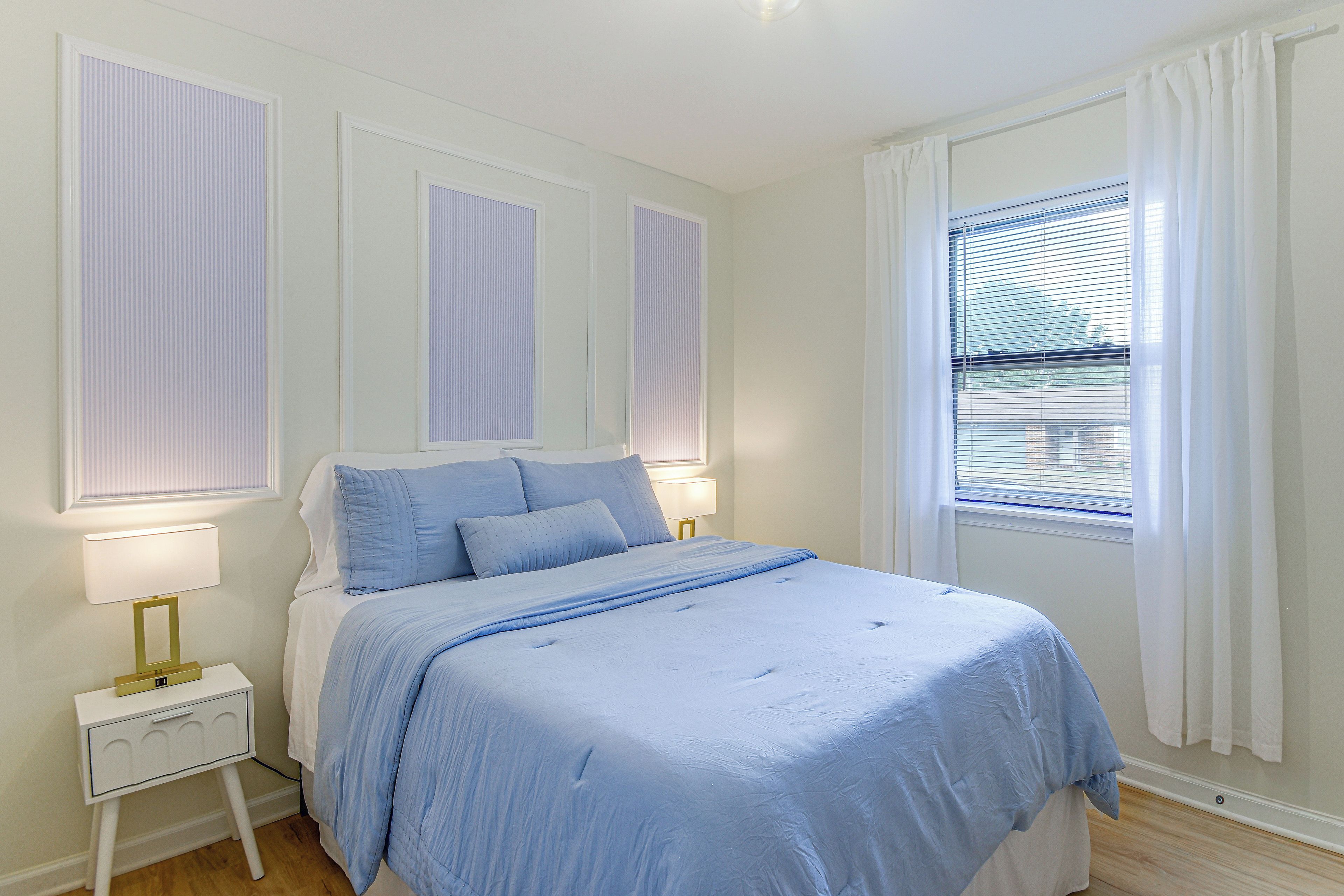 A bedroom with a bed, bedside lamps, a nightstand, and a window with blinds.