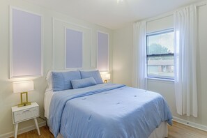 A bedroom with a bed, bedside lamps, a nightstand, and a window with blinds.