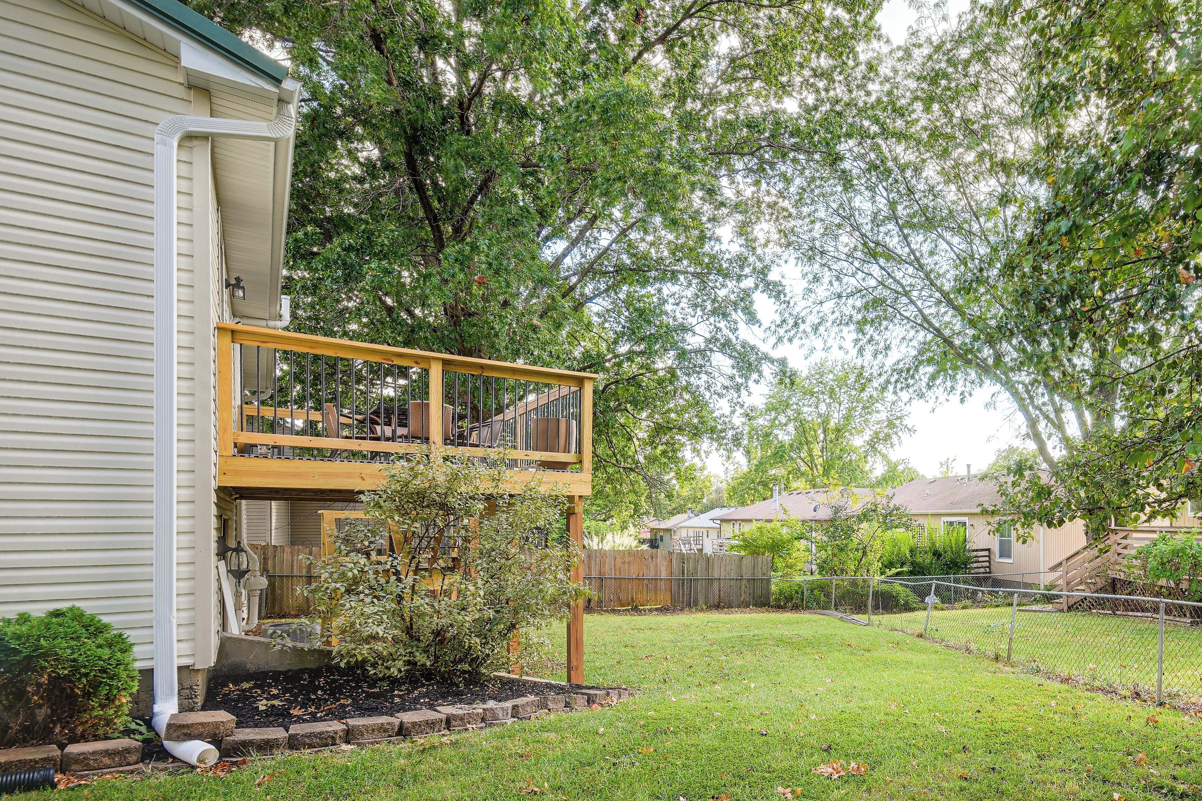 A residential property with a two-story deck, a fenced yard, and mature trees.
