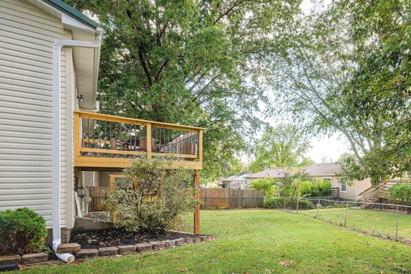 A residential property with a two-story deck, a fenced yard, and mature trees.