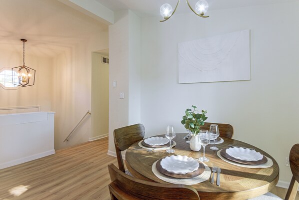 Un coin repas avec une table ronde en bois, dressée pour quatre personnes, entourée de chaises.