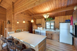 A wooden cabin interior with a kitchen area, bar seating, and a large island. - Lake Tapps Getaway w/ Private Fishing Dock! (Bonney Lake)