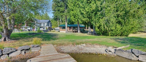 A wooden dock leading to a small pond with a grassy area and a building in the background.