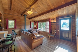 A log cabin interior with a wooden ceiling, a fireplace, a sofa, and a dining area. - Lake Tapps Getaway w/ Private Fishing Dock! (Bonney Lake)