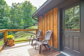 Um deck de madeira com cadeiras Adirondack, uma pequena mesa e um arranjo de flores.