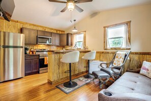 A kitchen with wooden cabinets, stainless steel appliances, and a bar area with two high chairs. - Deer Lodge Cabin by the French Broad River (Brevard)