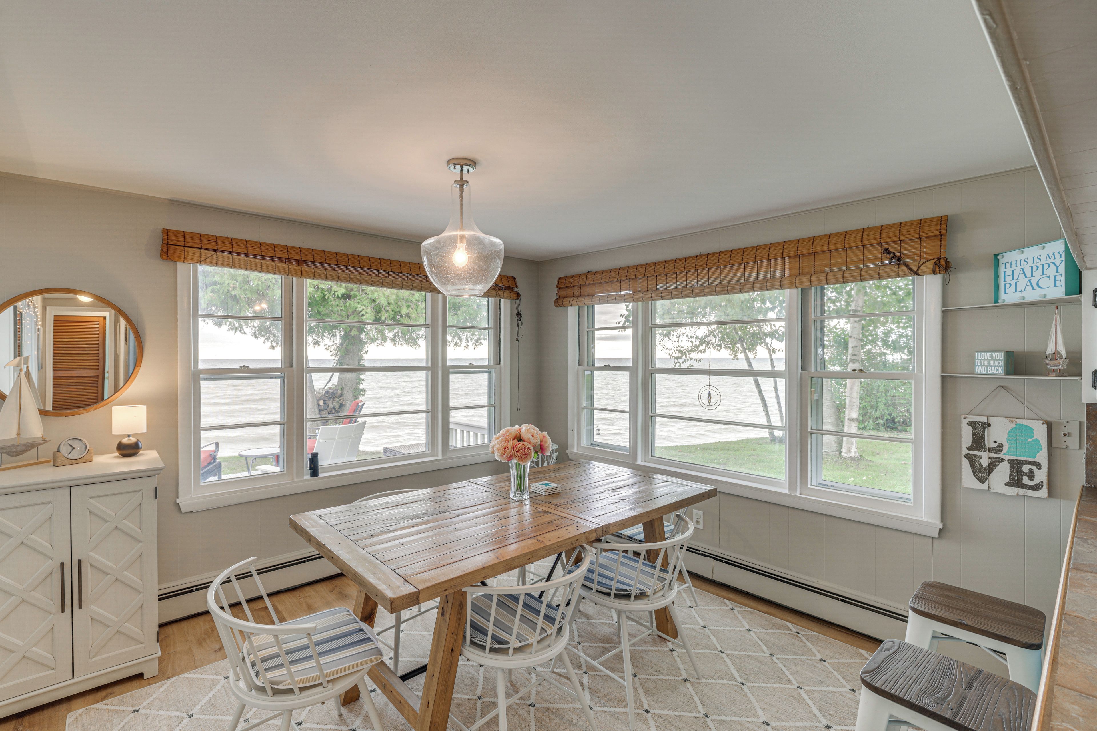 A room with a wooden table, chairs, a hanging light fixture, and large windows with views of the outdoors.