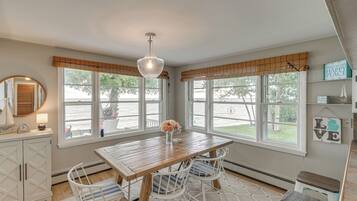 A room with a wooden table, chairs, a hanging light fixture, and large windows with views of the outdoors.