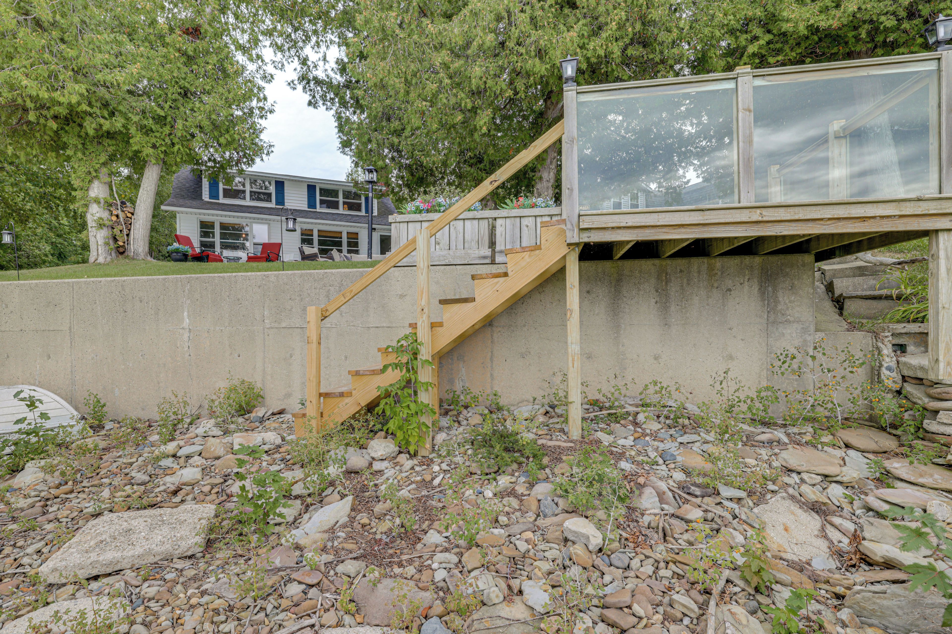 A wooden staircase leading to a glass-enclosed upper level, surrounded by a concrete wall and a rocky ground.