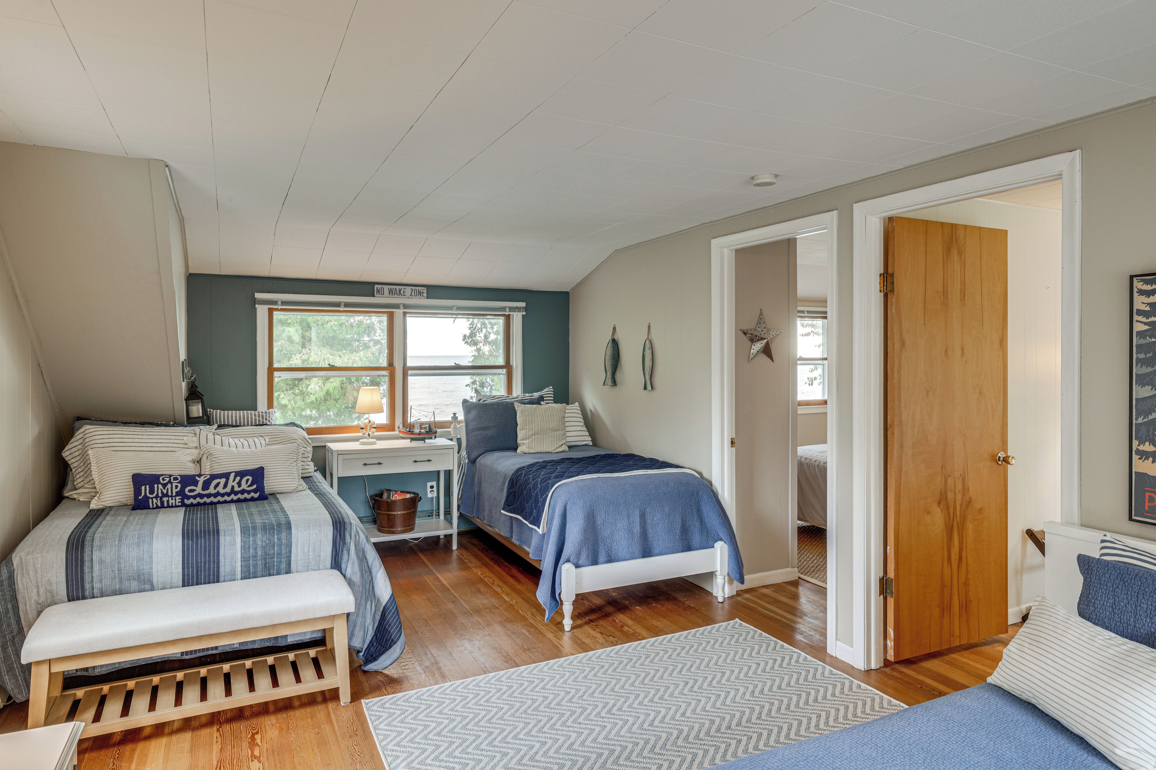 Un dormitorio con dos camas, un escritorio, una banca y una puerta que da a otra habitación.
