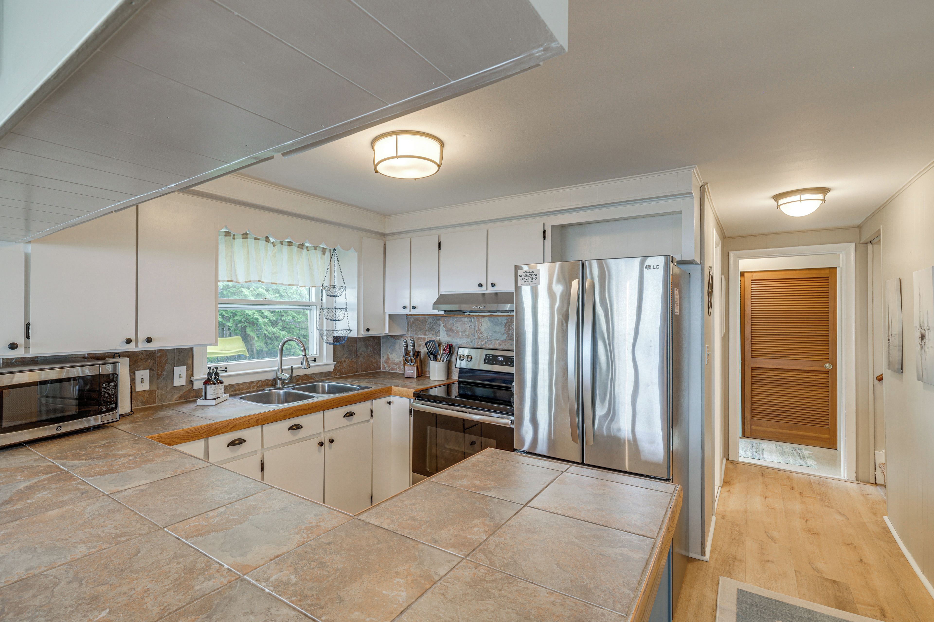 A modern kitchen with a stainless steel refrigerator, double sink, and a large window.