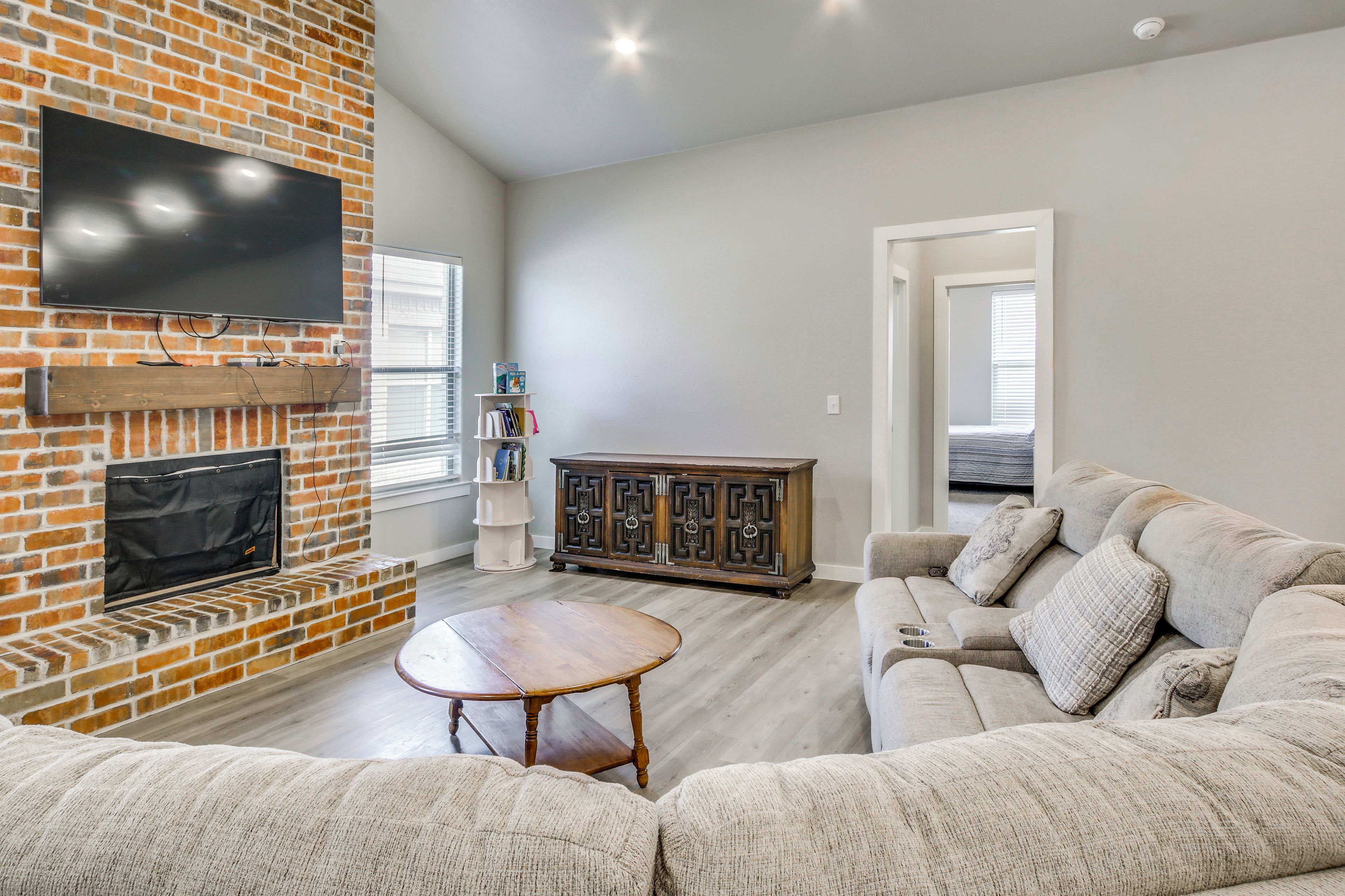 A living room with a brick fireplace, a flat-screen TV, a wooden coffee table, a sofa, and a bookshelf.