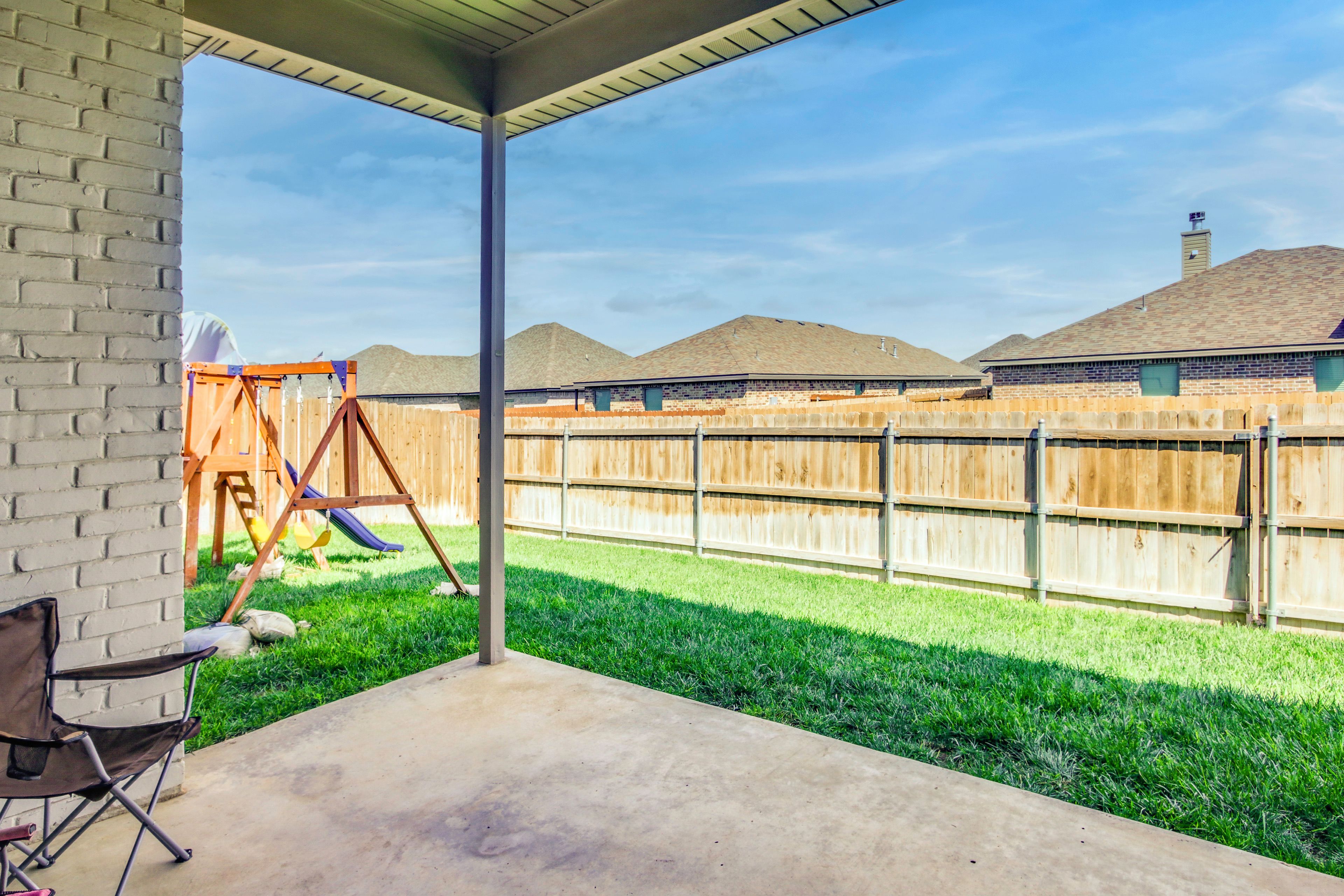 A covered patio area with a concrete floor, a wooden fence, and a grassy yard.