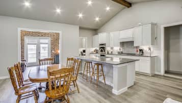 A spacious kitchen with white cabinets, a large island, and a dining area with wooden chairs.