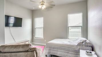 A bedroom with a bed, a bench, a desk, a ceiling fan, and a TV mounted on the wall.